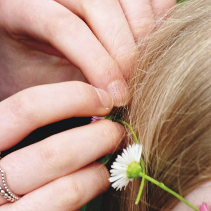 daisy chain hair crown being put in a girls hair close up shot